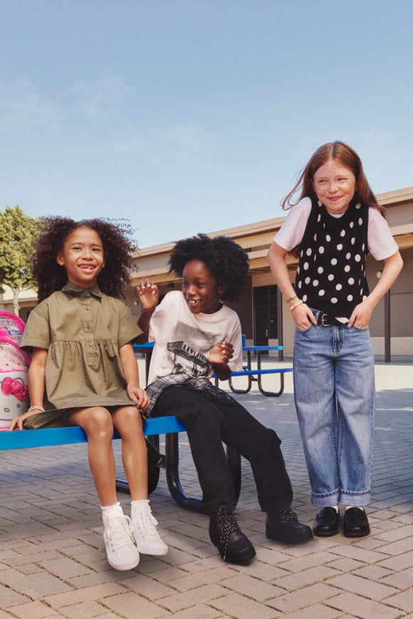 Three children in casual back to school outfits smile and laugh together on a blue bench.