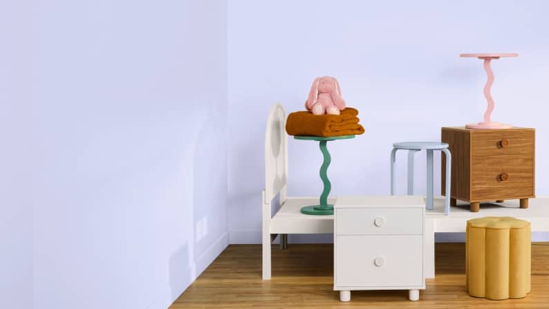 A white bed frame, colorful wavy side tables and a wooden nightstand on a wood floor. Reads: From twenty-nine ninety-seven. Kid-approved furniture.