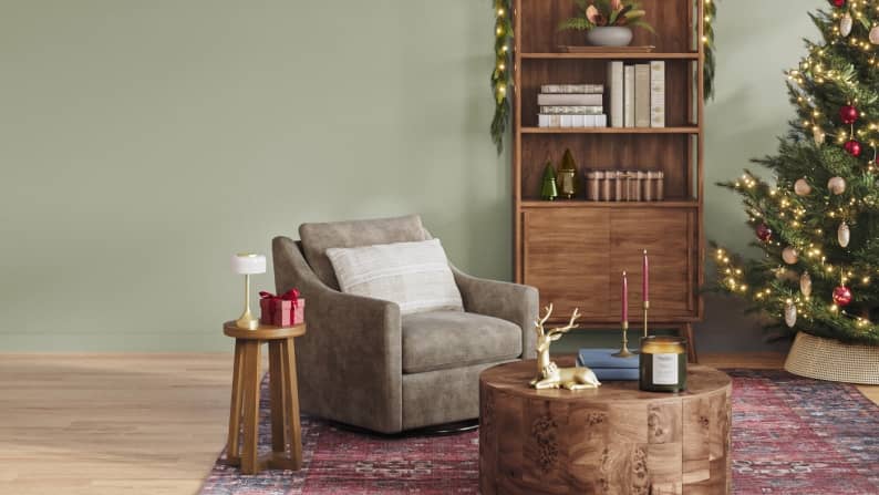 A sage green living room features an accent chair, coffee table, Christmas tree and festive decor.