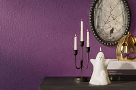 Image of dark console table decorated with a ghost, skull, and gold jack-o-lantern. The wall is a deep purple.