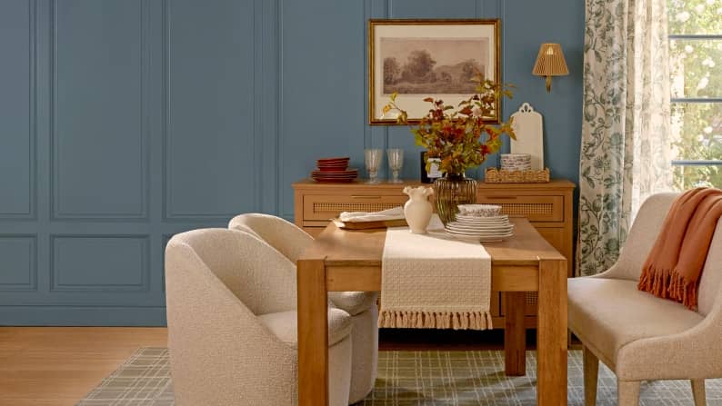 A dining room is set with a wooden table and console with decor and dinnerware. A beige upholstered bench and chairs accent the room.