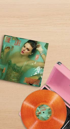 Image of Taylor Swift’s new album titled “The Life of a Showgirl” on a light wooden surface next to an orange record.