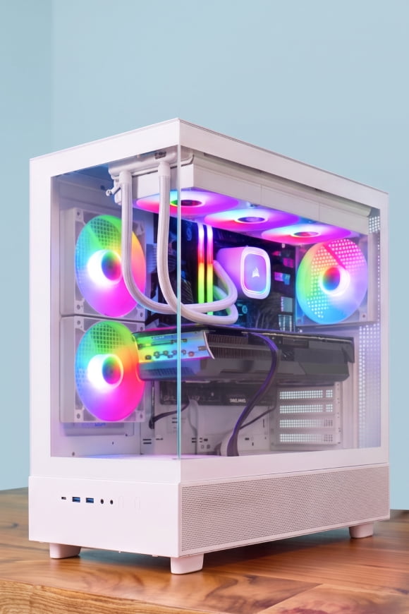 White gaming desktop PC tower with glass side panel and multicolor RGB fans on a wooden surface.