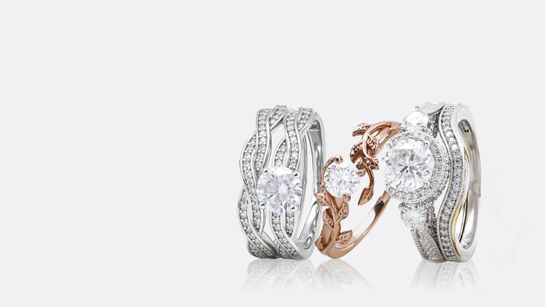 Two diamond wedding and engagement ring sets and a single wedding band are leaning against one another.