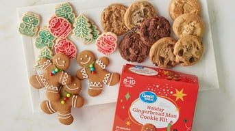 Great Value holiday gingerbread man baking kit is shown next to a plate of decorated cooked gingerbread men and an assortment of chocolate chip cookies.