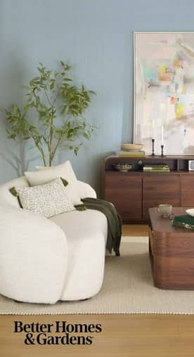 A living room is shown with a beige sofa, a wood console and matching coffee table, an abstract painting and an indoor tree.
