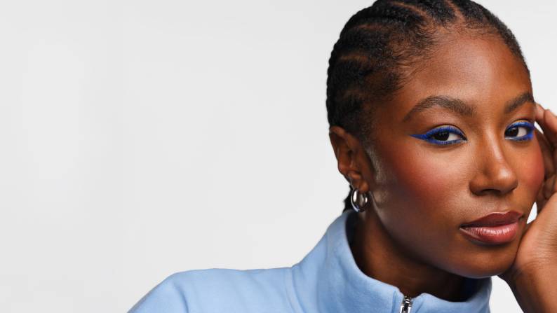 Lifestyle shot of model wearing blue eye liner with text: Beauty trend alert! The color to wear now.