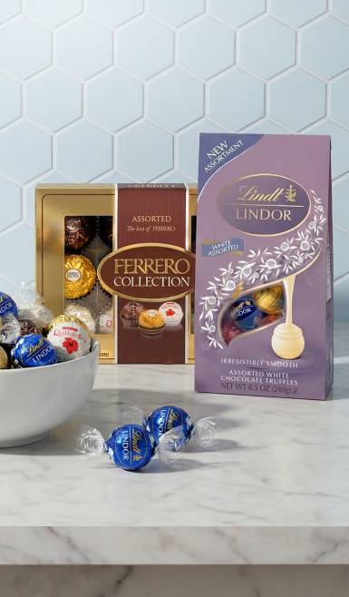 A white bowl of Lindt truffles next to a box of Ferrero Rocher chocolates and a bag of Lindt truffles.