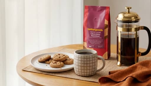 Bettergoods Chocolate Hazelnut ground coffee bag with a mug of coffee, cookies on a plate and a French press on a table.