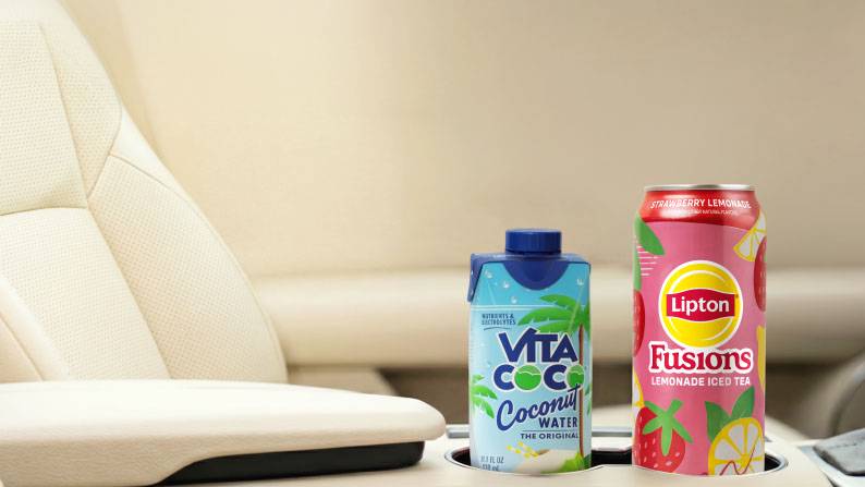 A Vita Coco coconut water carton next to a can of Lipton Fusions strawberry lemonade iced tea in a car’s center console cupholders.