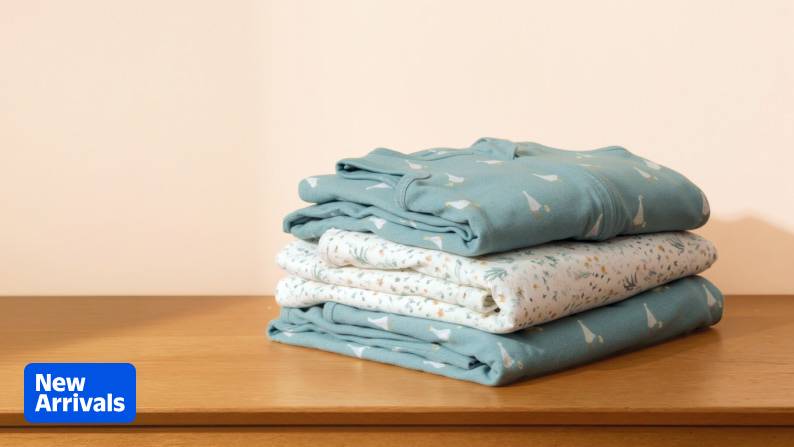 A stack of folded patterned blankets and swaddles on a wooden tabletop. New Arrivals