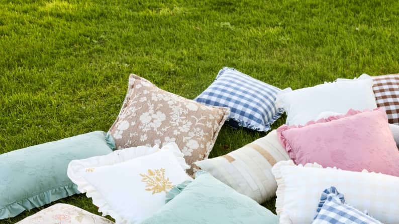 A mix of decorative pillows with various patterns laying on the grass.