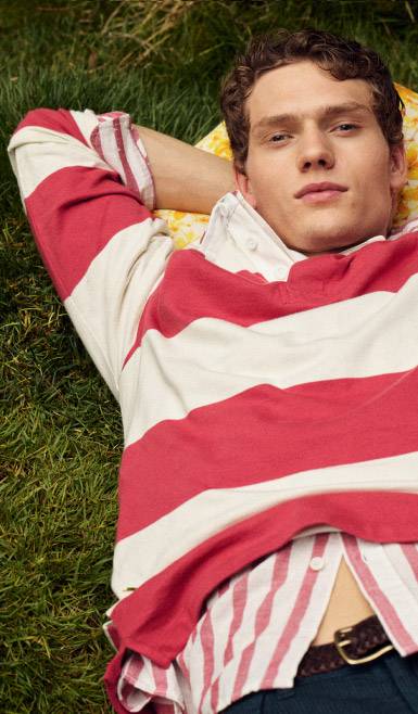 A man in jeans and a red-and-white rugby shirt over a red-and-white button-up, laying down on the grass.