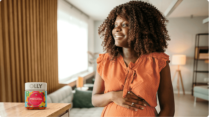 An expecting mother poses next to a bottle of Olly Prenatal gummy supplements.