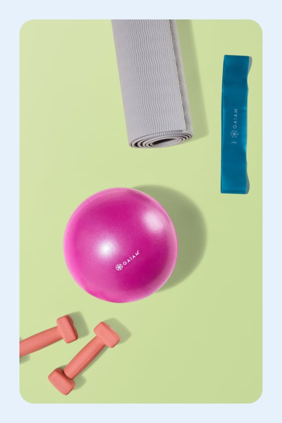 A pink balance ball, grey yoga mat, blue exercise band, and orange hand weights on a green background.
