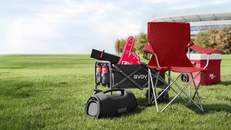 A stadium lawn is shown with a chair, cooler, onn. speaker, wagon.