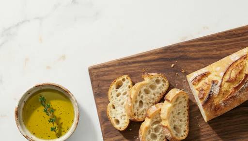 A bread loaf is shown sliced next to a bowl of olive oil for dipping.