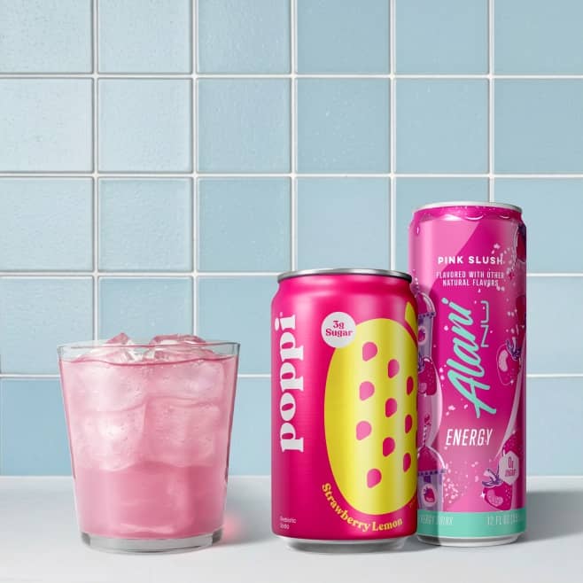 A can of poppi and a bottle of Sparkling Ice water sit on a counter next to a glass containing a pink drink.