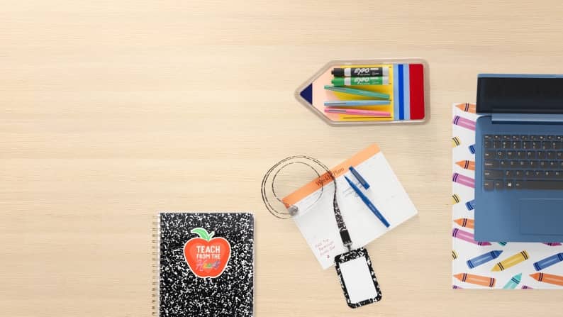 Pencils, markers, pens, a lanyard, a notebook, and a laptop on a wood desk.