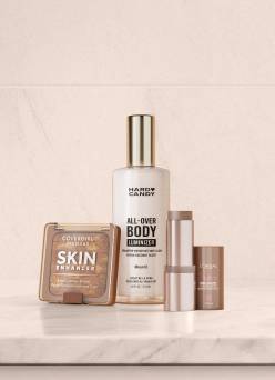 Close-up of bronzer compact, body luminizer bottle, and liquid highlighter on neutral stone surface.