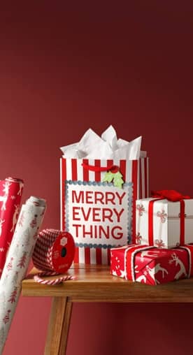 Image of a wooden bench with holiday gift bags, wrapping paper and ribbons.