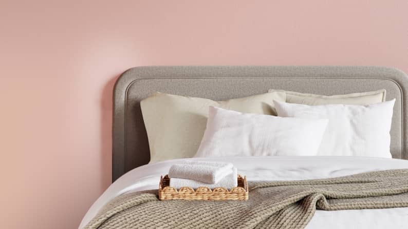Towels in a rattan tray on a bed with a gray headboard and white bedding.