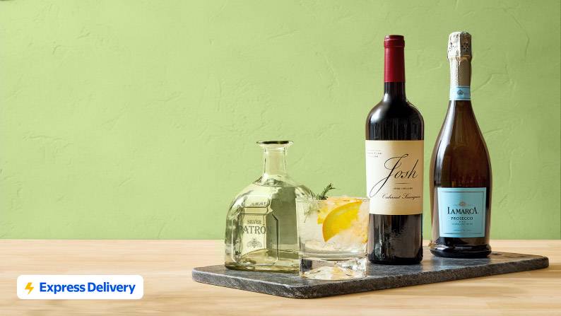 :A bottle of Patrón silver tequila, a bottle of Josh cabernet sauvignon, and a bottle of La Marca prosecco on a marble tray.