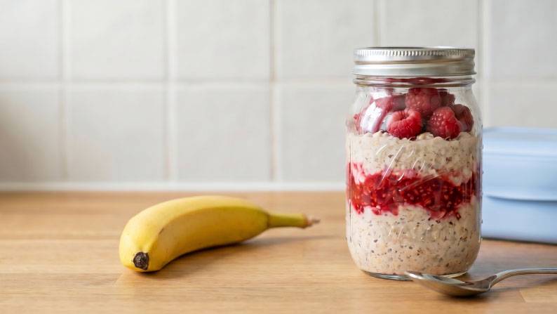 From $2.98. A jar of overnight oats with raspberries on a wooden counter next to a banana and a spoon.