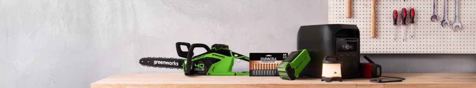 Greenworks chainsaw, portable power station, battery pack and lantern on a wooden workbench in a workshop.