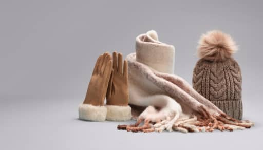 Women’s tan faux suede gloves, tan striped blanket scarf and a brown cable knit pom beanie are shown.