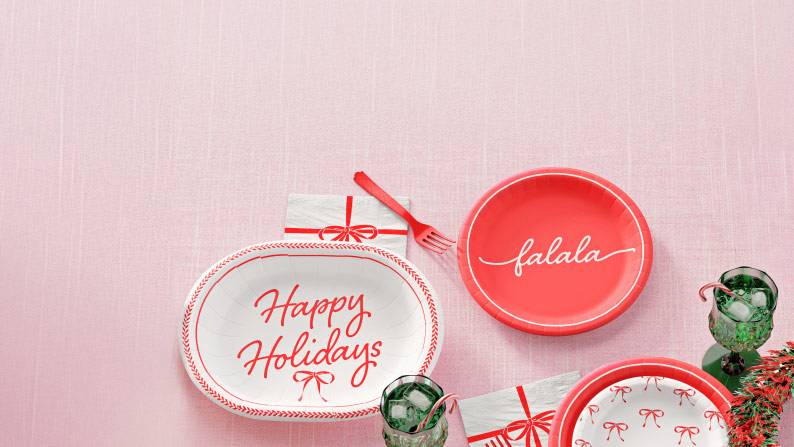 Image shows red and white holiday tableware with red cutlery, red napkins, and green glasses.