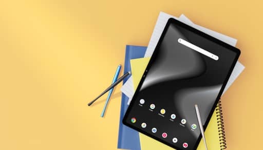 A digital tablet displaying abstract architectural shapes sits on a pile of notebooks and lined paper next to pens.