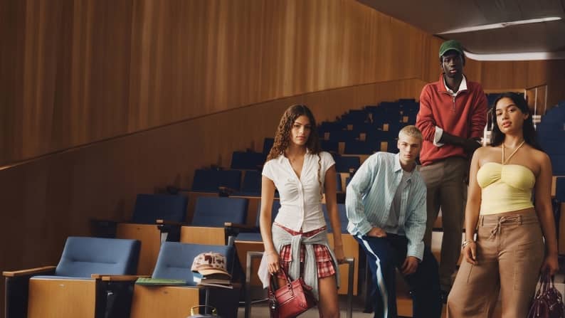 A group of four young people wearing stylish clothes is standing in a lecture hall.