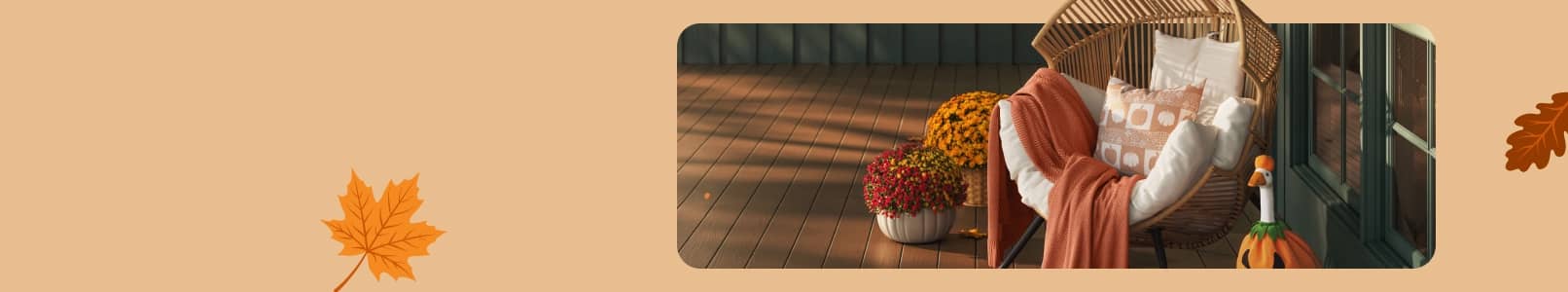 Outdoor lounge chair with pillow and rust throw beside a basket of fall flowers and decorative pumpkin on a wooden patio.