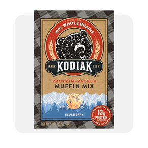 Image shows a box of Kodiak Protein-Packed Blueberry Muffin Mix made with whole grains, featuring a bear logo and a muffin image on the packaging.