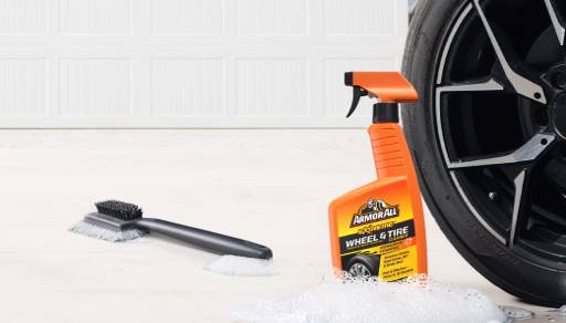 A tire brush and cleaning fluid next to a tire.