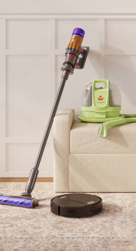 A stick vacuum, carpet cleaner, and robo vacuum is showing with a cream upholstered bench and a rug.