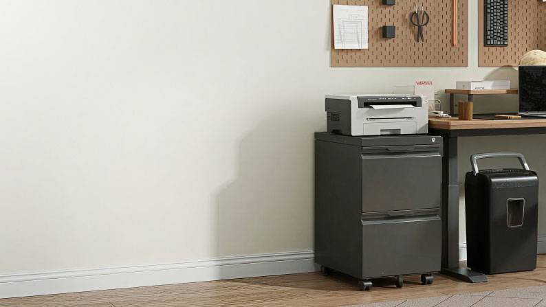 A well-organized office with grey cabinets and fully stocked with office supplies including a printer, keyboards and a laptop.