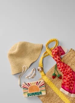 A beach bag, straw hat, printed pouch, and jewelry are layered.
