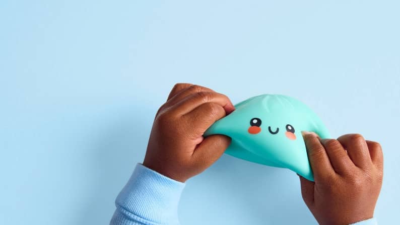 Child hands stretch a teal squishy toy with a smiling cartoon face and pink cheeks.
