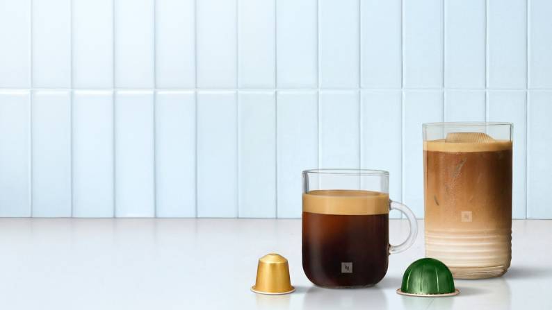 Two cups of coffee are shown. One has a foamy head and the other has creamer in it. Two Nespresso pods are in the foreground.