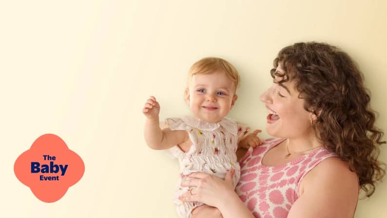 A woman holds a smiling baby. The Baby Event
