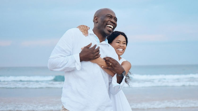 A man and his partner pose with each other on the beach.