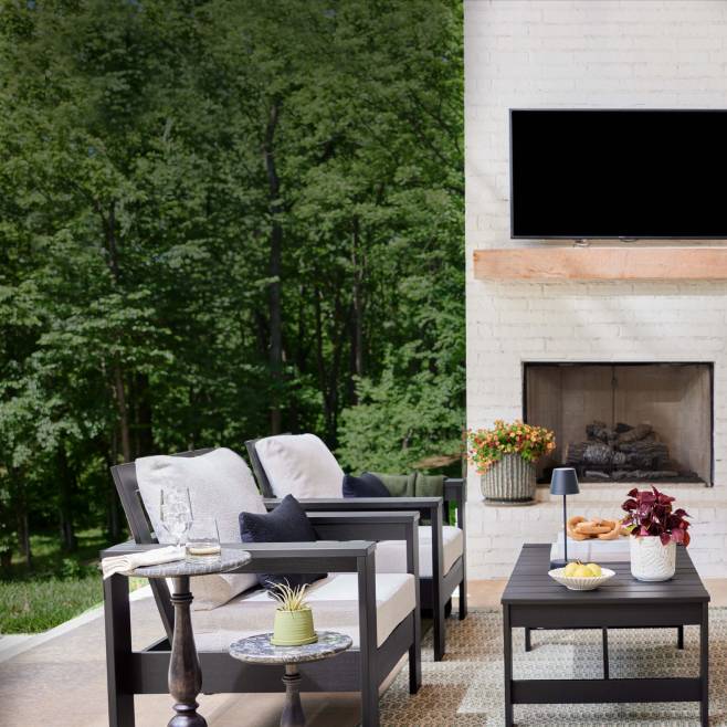 Black metal-framed chairs with white cushions and a matching coffee table on a patio. Pedestal tables and outdoor potted plants. An outdoor rug.