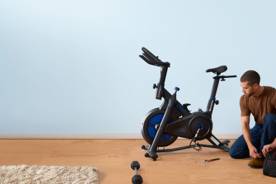 An image of a person kneeling in front of an exercise bike.