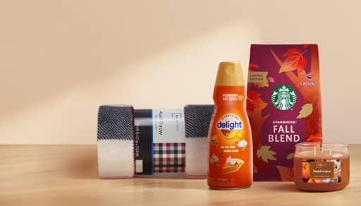 A plaid blanket, International Delight pumpkin spice creamer, Starbucks fall blend coffee and pumpkin spice candle on a wooden table.