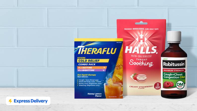A pack of Hall’s cough drops, Theraflu and a bottle of Robitussin on a white stone counter with a blue tiled wall behind them.