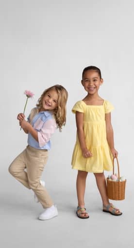 A little boy wearing a colorful shirt and khakis is standing next to a little girl wearing a yellow dress.