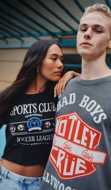 A young woman and a young man wearing graphic tees are posing together.