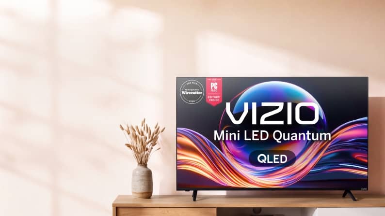 Award badges and Vizio Mini LED Quantum QLED TV on a wooden console with a vase of dried flowers.
